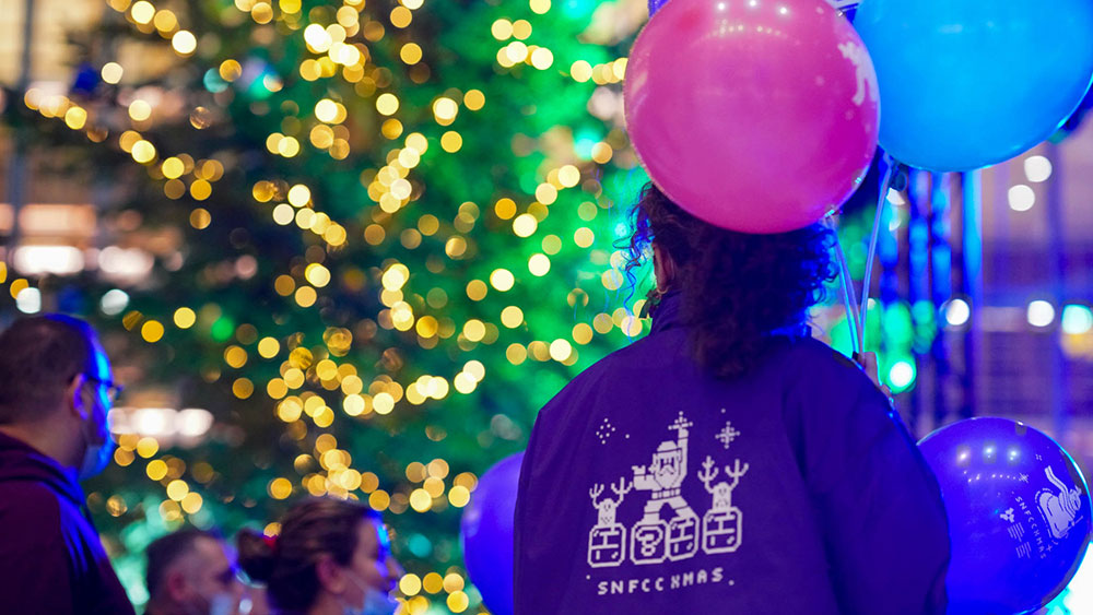 Μια γυναίκα που κρατάει μπαλόνια κοιτάζει τα στολισμένα δέντρα