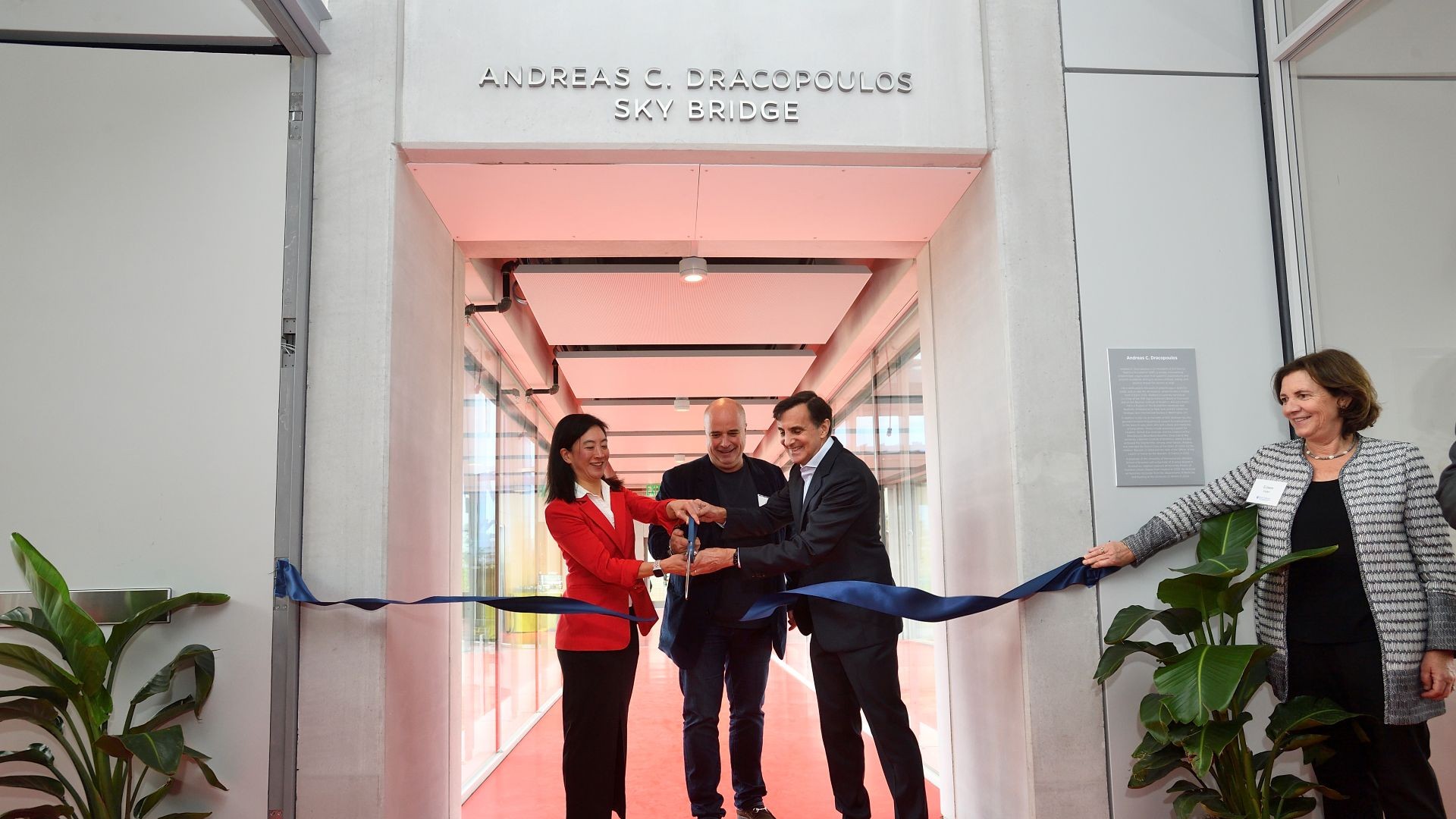 One woman and two men cut a ribbon at the Andreas C. Dracopoulos Sky Bridge inaguration. 